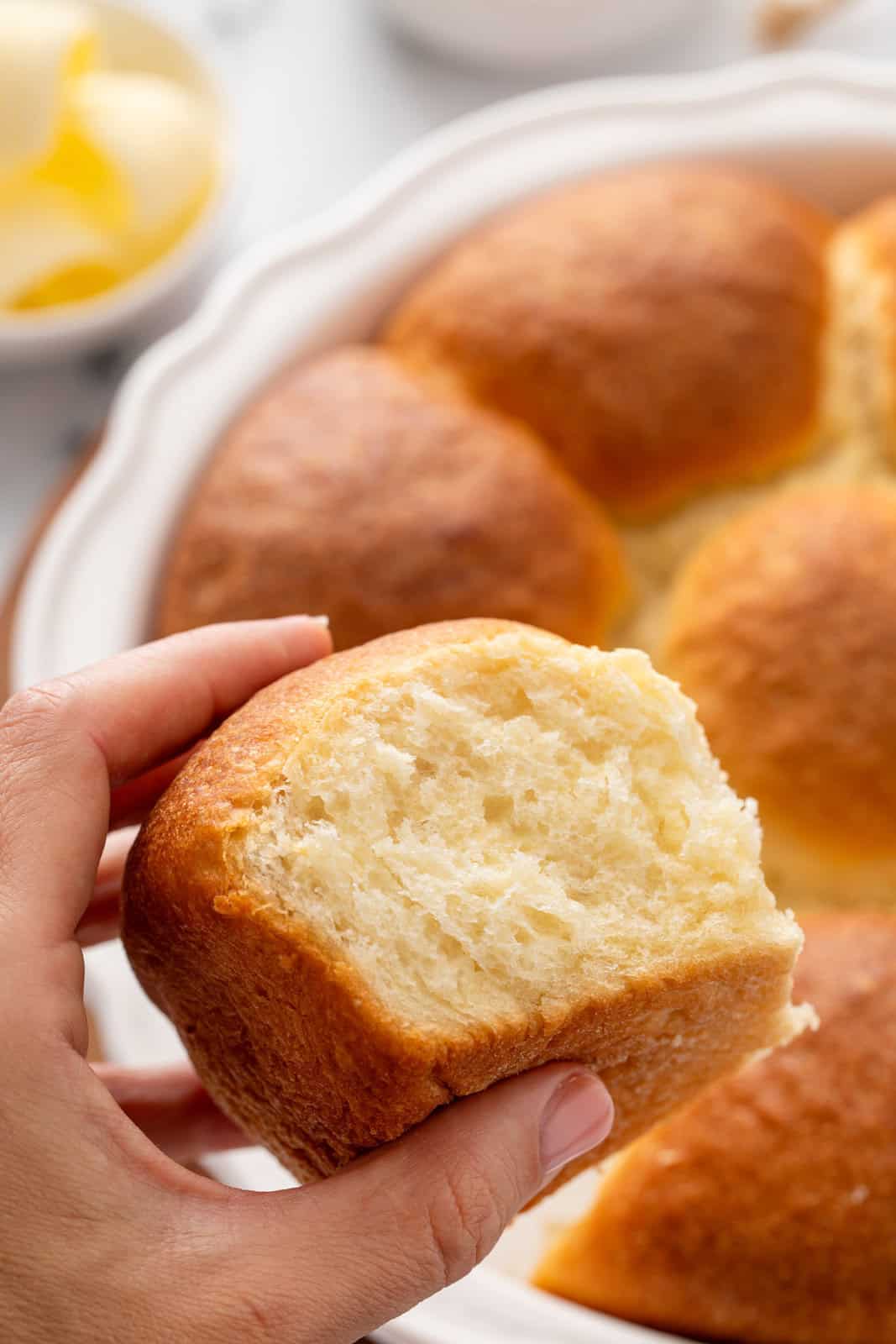 Hand holding up a refrigerator roll with the pan of rolls in the background.