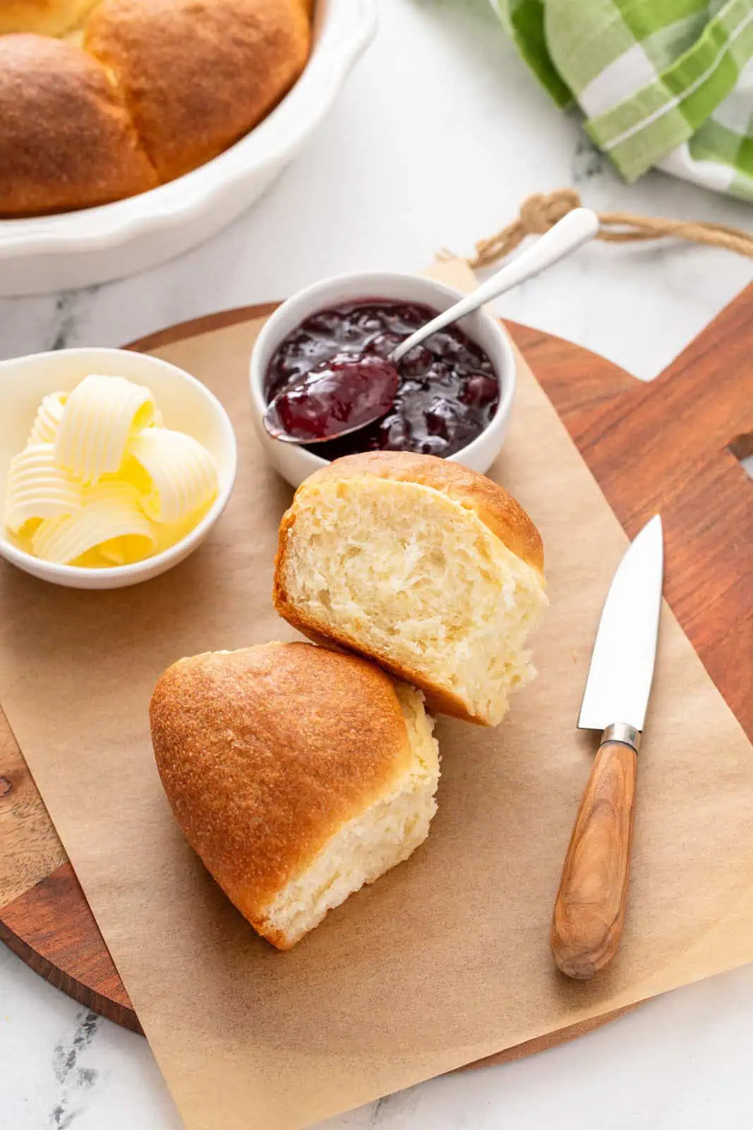 Two refrigerator rolls on a wooden board next to butter and jam.