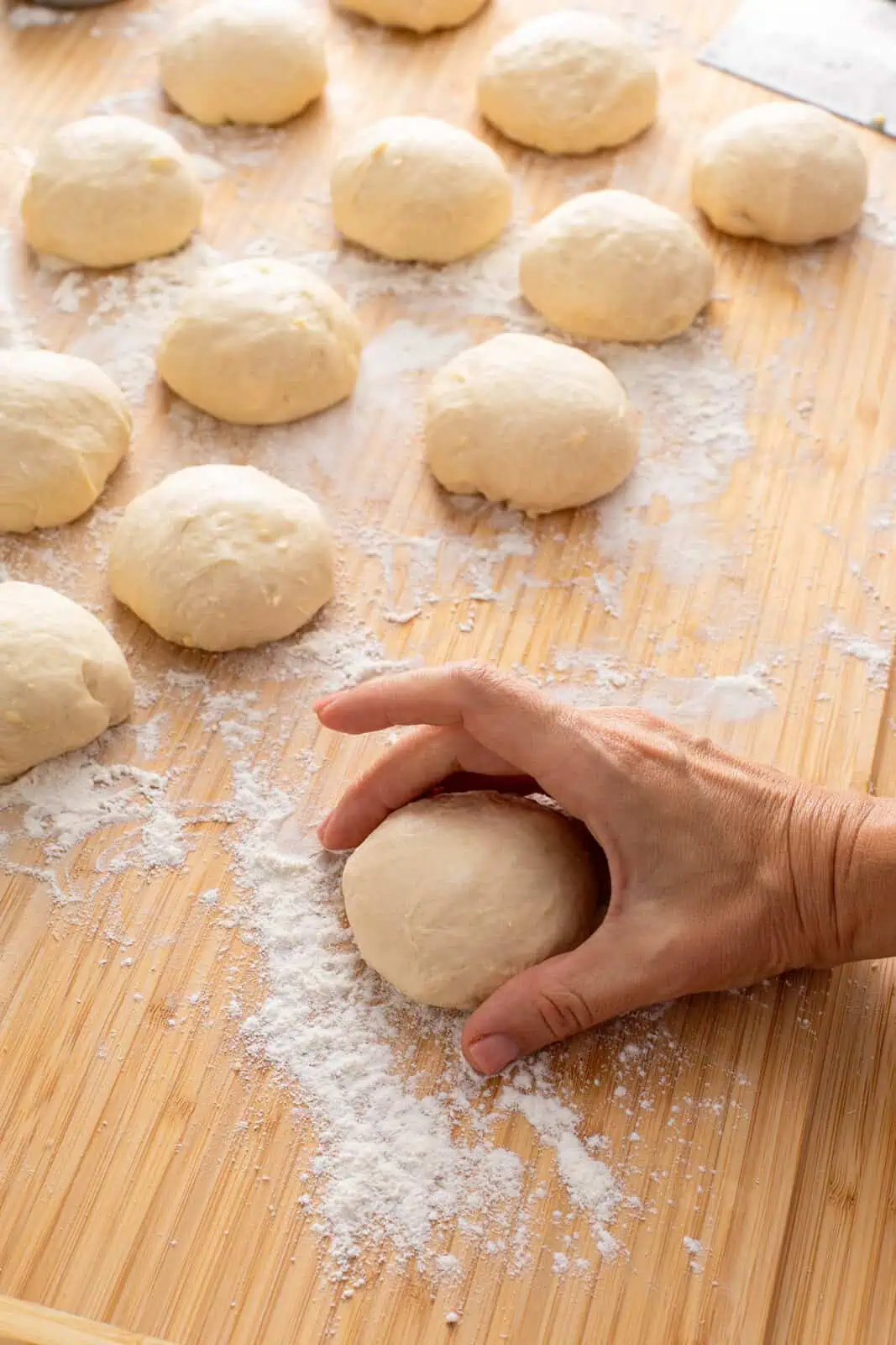 Hand shaping portions of yeast dough into rolls.