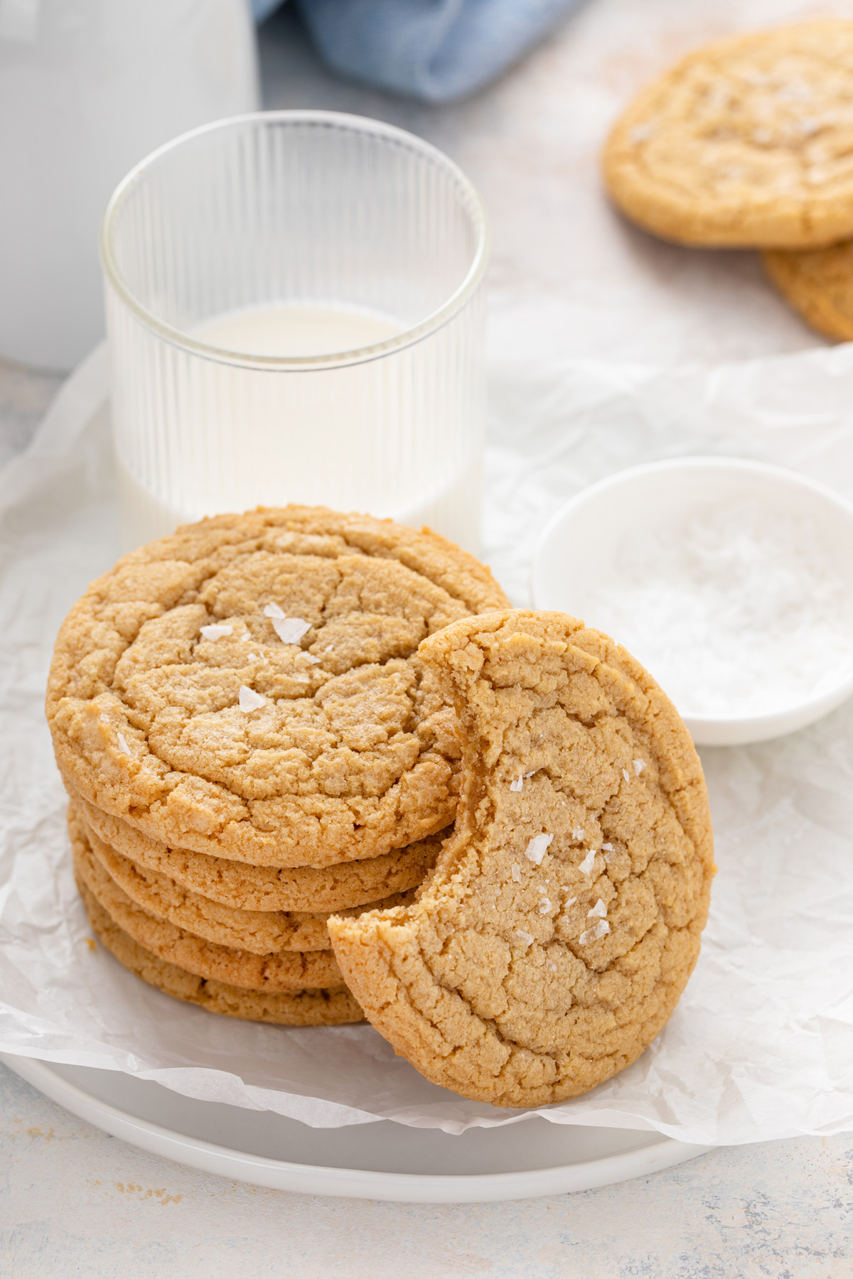 Stack of chocolate chipless cookies next to a glass of milk with a cookie with a bite taken from it leaning against the stack.