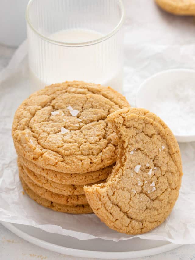 Stack of chocolate chipless cookies next to a glass of milk with a cookie with a bite taken from it leaning against the stack.