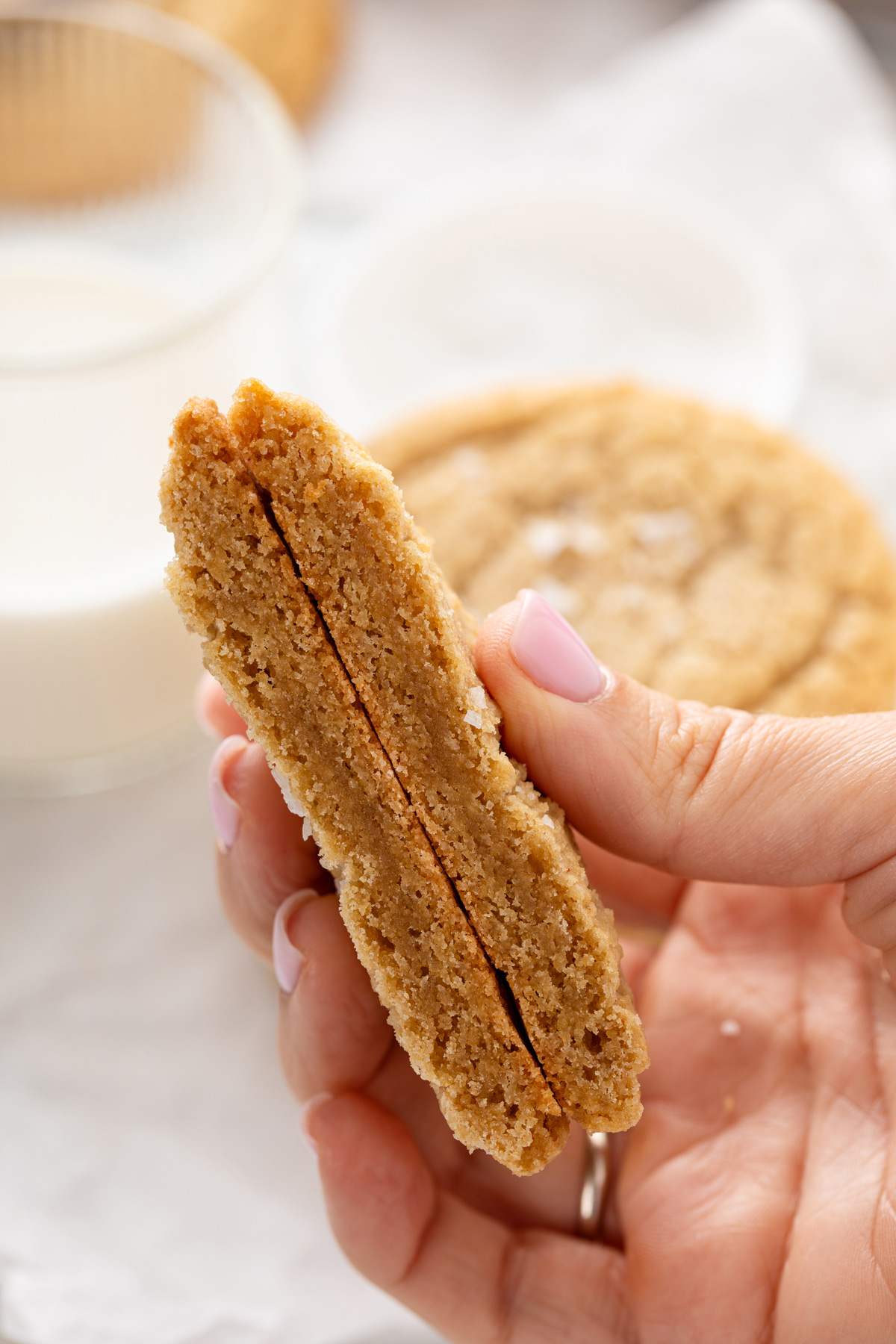 Hand holding up a halved chocolate chipless cookie to show the chewy texture.