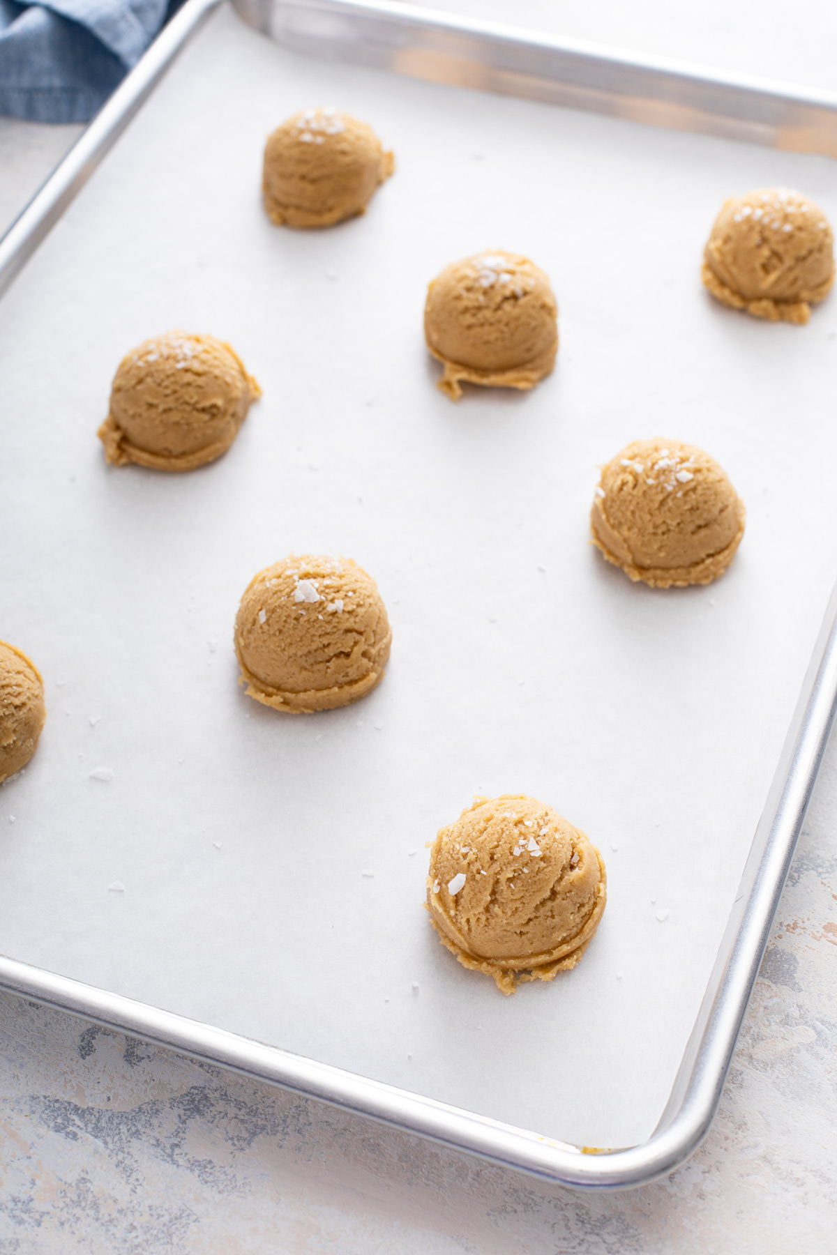 Balls of chocolate chipless cookie dough on a lined baking sheet, ready to go in the oven.