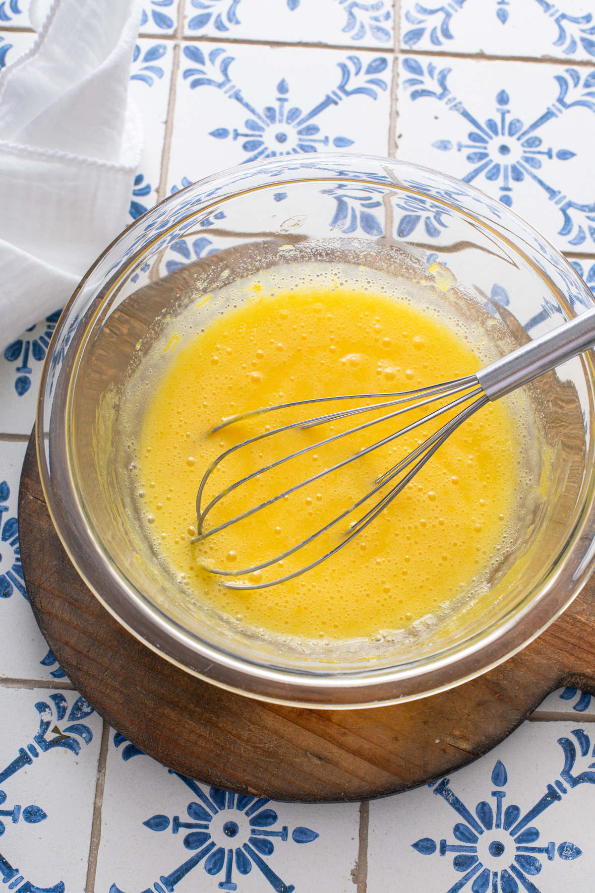 Gelatin and lemon zest whisked into lemon curd in a glass bowl.