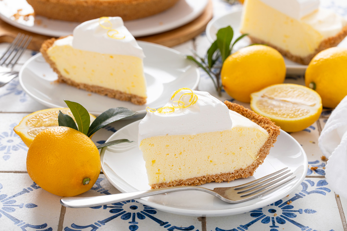 Two white plates on a blue and white countertop, each holding a slice of lemon chiffon pie.